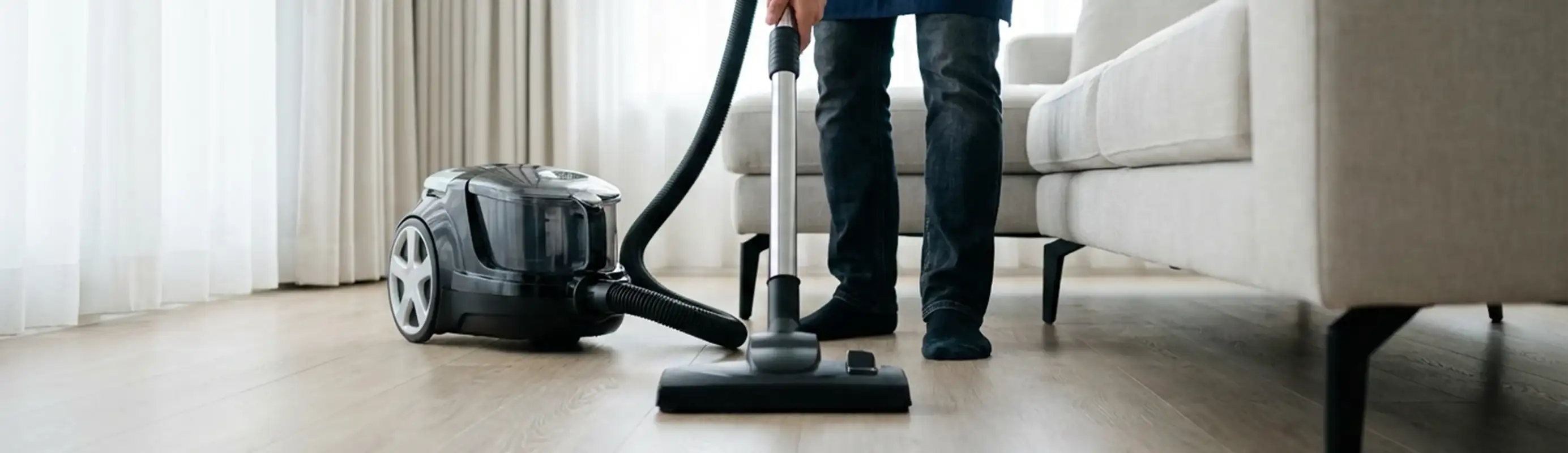 Professional house cleaner vacuuming a living room floor with a canister vacuum cleaner, Stockton, CA.