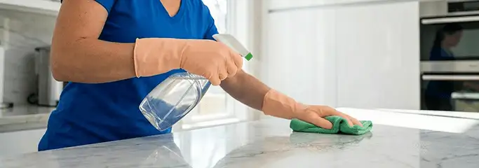 Maid service worker spraying and wiping a kitchen countertop with a microfiber cloth for sanitizing, Stockton, CA.