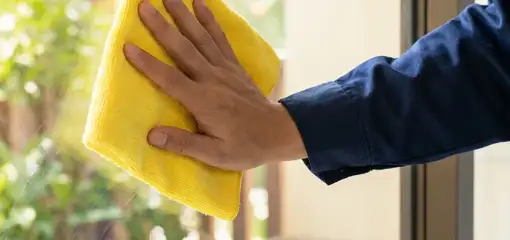 House cleaner wiping a glass window with a yellow microfiber cloth for streak-free cleaning, Stockton, CA.